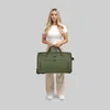 A woman stands holding a green duffle bag. Produktbild-Vorschau