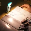A person is reading a book with a small LED light attached to the page. Produktbild-Vorschau