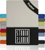 A product image showcasing a beige fitted sheet with a black band at the top corner displaying the brand name and product type. Several other colored fitted sheets are stacked vertically on the left and right sides of the main product. Produktbild-Vorschau