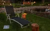 A lounge chair is set up on a grassy lawn next to a pond, with outdoor lighting and seating in the background. Produktbild-Vorschau
