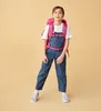A young girl wearing a backpack and overalls, standing against a plain background. Anteprima dell’immagine prodotto