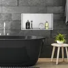 A modern bathroom with a black bathtub, grey tiled walls, and a built-in shelf with toiletries. Náhled obrázku produktu