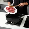 A person is adding raw meat to a square cooking pot on a stovetop. Náhled obrázku produktu