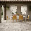 An outdoor dining set with orange chairs and a white table on a stone patio, under a tiled roof. Produktbild-Vorschau