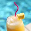 A close-up of a tropical drink with ice, a pineapple wedge, and a pink straw, with a blurred blue background that appears to be a swimming pool. Produktbild-Vorschau