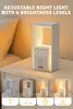 A white bedside lamp with a digital clock display is shown on a nightstand next to a yellow pillow. Below the main image, there are four smaller images showing the lamp at different brightness levels. Produktbild-Vorschau