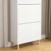 A close-up view of a white shoe cabinet with wooden legs, placed against a wall with curtains. Produktbild-Vorschau