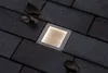 A square, recessed LED light fixture is embedded in a dark brick pathway. A few dry leaves are scattered on the bricks around the light. Produktbild-Vorschau