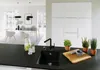 A modern kitchen with a black sink and faucet in the foreground, and a dining area in the background. Produktbild-Vorschau