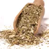 A wooden scoop filled with dried mate tea leaves and stems, with some spilled onto a white surface. Voir les images du produit