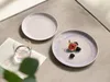 Two plates with fruit and a glass of water on a textured surface. Produktbild-Vorschau