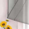 A close-up of a gray sheer roller blind with decorative straps, partially covering a window. In the foreground, there are several bright yellow sunflowers. Produktbild-Vorschau