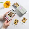 A person is holding a smartphone connected to a portable photo printer, printing photos of themselves and a friend with a yellow flower. A yellow gerbera daisy is also in the scene. Náhľad obrázku produktu