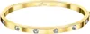 A gold-colored bangle bracelet with clear stones and a brand logo. Produktbild-Vorschau