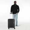 A man stands next to a black suitcase. Produktbild-Vorschau