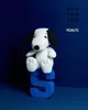 A Snoopy plush toy sitting on a blue letter 'S' against a dark blue background, with brand logos at the top right. Anteprima dell’immagine prodotto