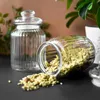 Two glass jars are on a dark surface, one upright and empty, the other lying on its side with its contents spilled. Produktbild-Vorschau