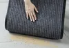 A hand is shown touching a rolled-up doormat on a tiled floor with some dirt scattered around. Anteprima dell’immagine prodotto