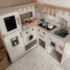 A wooden children's play kitchen with various accessories, including a refrigerator, washing machine, oven, sink, stovetop, and a basket of toy food. Podgląd zdjęcia produktu