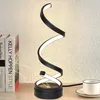 A modern black spiral LED desk lamp is displayed on a wooden surface next to two books and a white coffee cup. Podgląd zdjęcia produktu