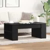A black coffee table is placed in a living room setting, in front of a sofa, with a plant in the background. Náhled obrázku produktu