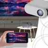 A hand holding a smartphone displaying a sunset scene, with a mini projector and a large screen in the background. Voir les images du produit