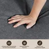 A person's hand is pressing into a dark gray fabric surface, demonstrating its softness and resilience. Below the fabric are three icons with accompanying German text. Voir les images du produit