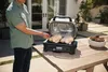 A person is preparing to cook two whole chickens in a Ninja Woodfire Pro XL electric grill outdoors on a wooden table. Voir les images du produit