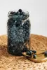 A glass jar filled with blueberries sits on a woven mat, with a small golden spoon holding a few blueberries next to it. Produktbild-Vorschau