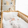 A baby lying in a crib next to a shelf with nursery items. Anteprima dell’immagine prodotto
