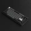 A black mechanical keyboard with gray and white keycaps is shown on a black surface. Produktbild-Vorschau