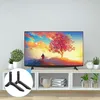 A pair of black TV stand feet are shown in a circular overlay against a backdrop of a TV stand with a TV on it, plants, and decorative items. Náhled obrázku produktu