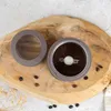 A coffee grinder and its lid are placed on a wooden board, surrounded by coffee beans. Náhľad obrázku produktu