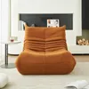 A cozy living room scene featuring a plush orange floor sofa in front of a modern fireplace with a small side table and a stack of firewood. Voir les images du produit