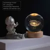 An astronaut figurine stands on a moon-like surface next to a glowing crystal ball displaying a galaxy. Produktbild-Vorschau