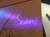 A close-up of a notebook with a secret message written in invisible ink, illuminated by a UV light. Produktbild-Vorschau