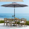 An outdoor dining set with chairs and a table under a large umbrella, situated on a patio overlooking a beach and the ocean. Produktbild-Vorschau