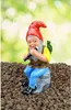 A garden gnome figurine sitting on a rock and playing a flute, with a small bird on its shoulder. The background is blurred green foliage. Produktbild-Vorschau
