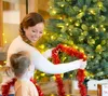 A woman and a child are decorating a Christmas tree with red tinsel. Produktbild-Vorschau