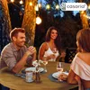 People enjoying a meal outdoors at night, illuminated by string lights. Produktbild-Vorschau