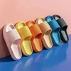 Sechs bunte Slide-Sandalen in Pink, Gelb, Orange, Beige, Blau und Schwarz, aufgereiht vor rosa Wand und blauem Boden Náhľad obrázku produktu