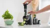 A person is using an electric vegetable slicer to slice a cucumber. A bowl of basil and a bowl of sliced cucumber are also visible. Náhled obrázku produktu