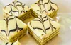 Close-up of several square-shaped pastries with white icing and dark chocolate drizzle, arranged on a white surface. Anteprima dell’immagine prodotto