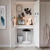A compact desk setup inside a white cabinet, featuring a laptop, lamp, and stool. Produktbild-Vorschau