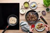 A top-down view of a person preparing fajitas on a wooden table, with ingredients and a stovetop. Produktbild-Vorschau