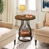 A round side table with two shelves, placed between two armchairs in a living room setting. Produktbild-Vorschau