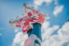A person's legs wearing jeans and inline skates are held up against a blue sky with clouds. Produktbild-Vorschau