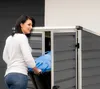 A woman is putting a blue trash bin into a dark gray storage box. Produktbild-Vorschau