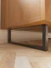 A close-up view of the bottom of a wooden cabinet with black metal legs, resting on a wooden floor. Produktbild-Vorschau