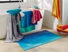A bathroom scene with towels draped over a bathtub and a bath mat on the floor. Produktbild-Vorschau